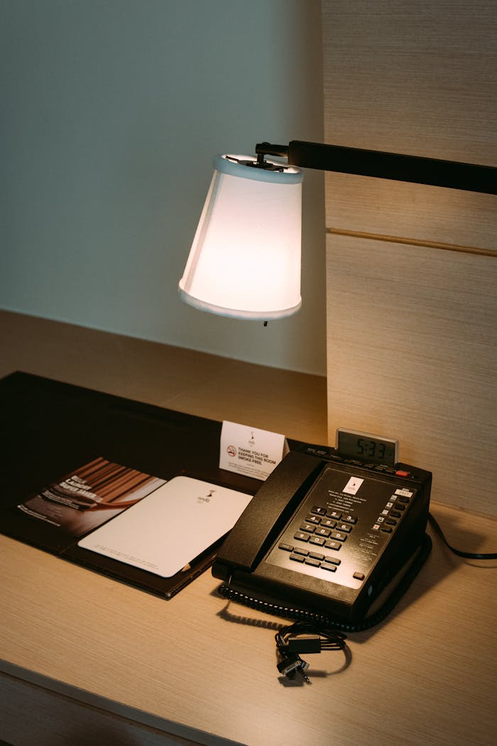 creative-02 A neatly arranged hotel desk featuring a telephone, lamp, and notebooks in a serene ambiance.