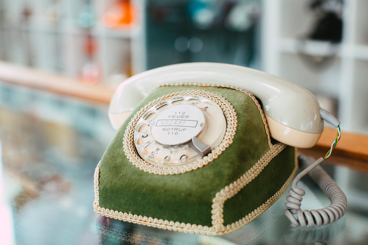 Close-up of a vintage rotary phone with green velvet cover on a glass table indoors.