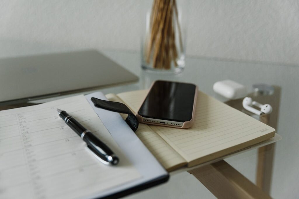 A minimalist desk setup featuring a smartphone, notebook, and wireless earphones for a modern, productive work environment.